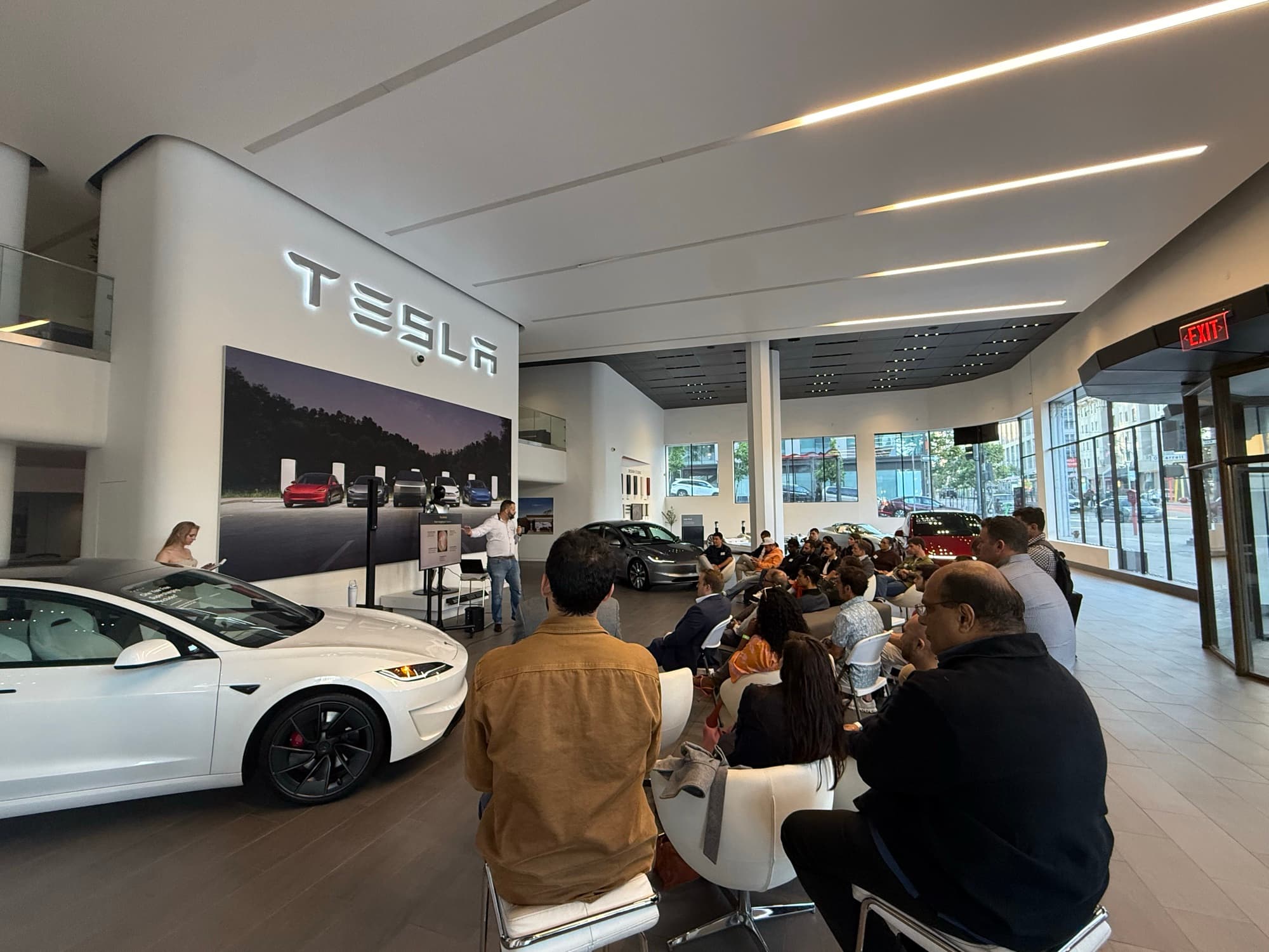 A Tesla Model 3 beside the audience at a San Francisco startup event in the Tesla showroom