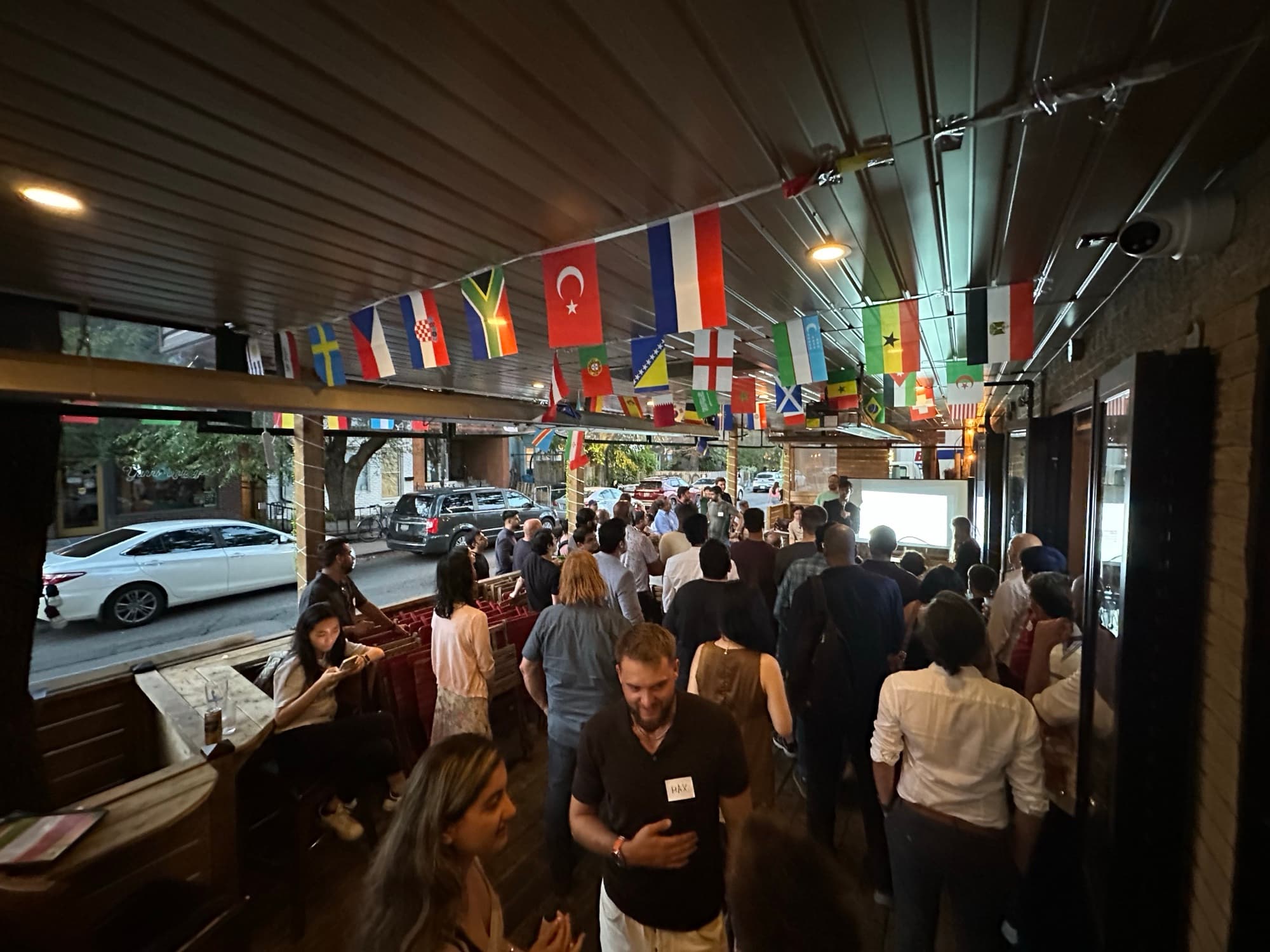 A packed Startup Valley pitch night on a Toronto patio — the crowd mingling under international flag bunting