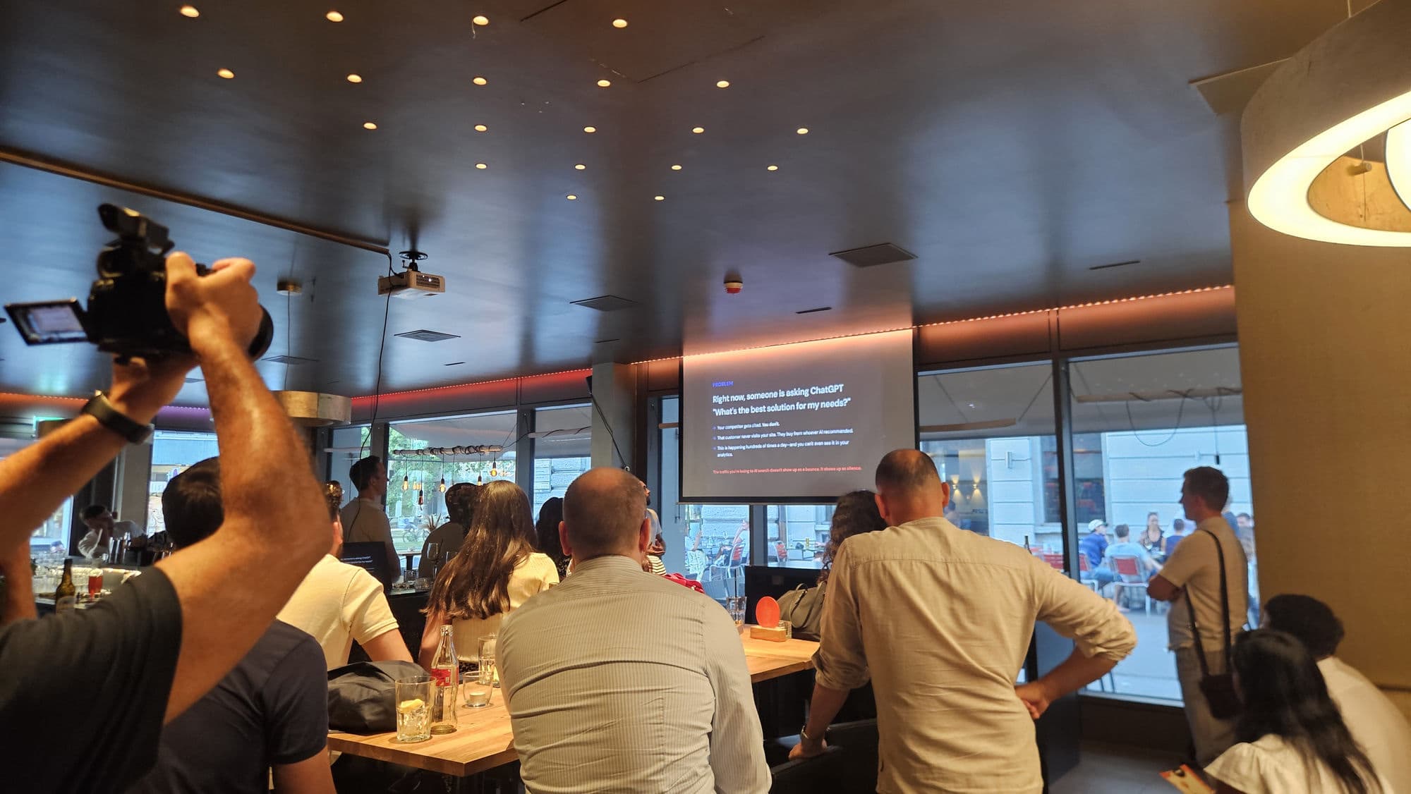 The crowd at a Zurich pitch night watching a live startup pitch, one attendee filming the presentation