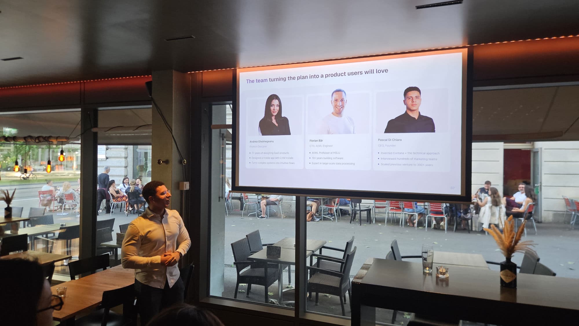 A founder pitching their startup live at a Startup Valley pitch night in Zurich, team slide on the screen behind them